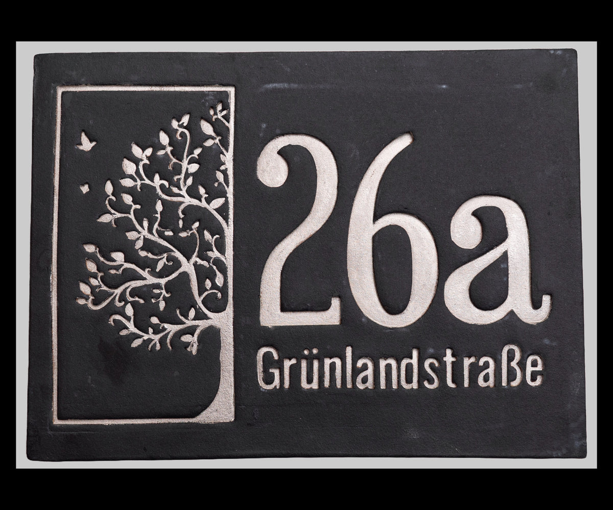 Schwarzes Hausnummernschild mit weißem Baum-Motiv und der Aufschrift 26a Grünlandstraße