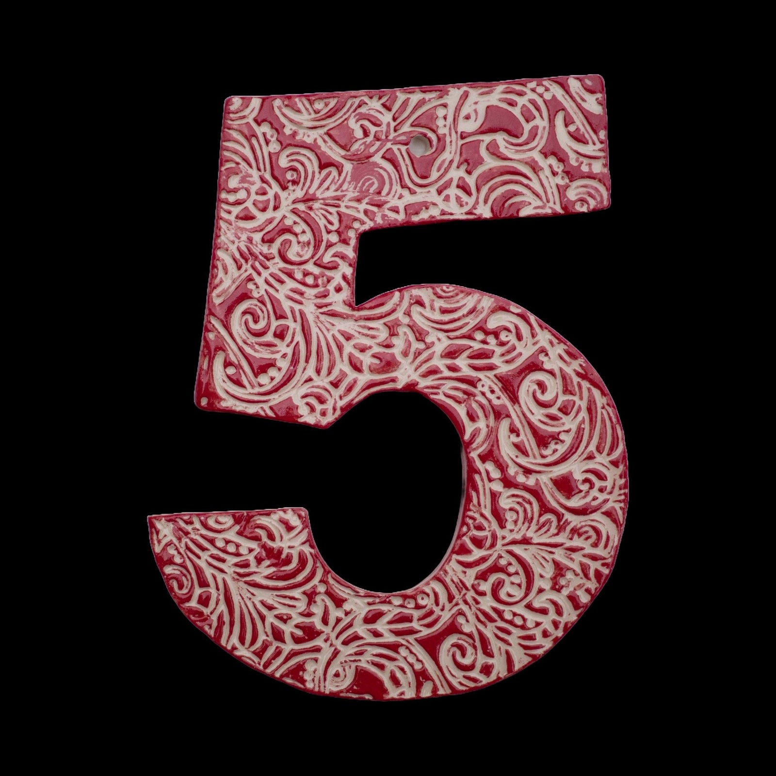Handgefertigte Keramik-Hausnummer „5“ in Rot mit weißen geprägten Ornamentmustern, vor schwarzem Hintergrund dargestellt.