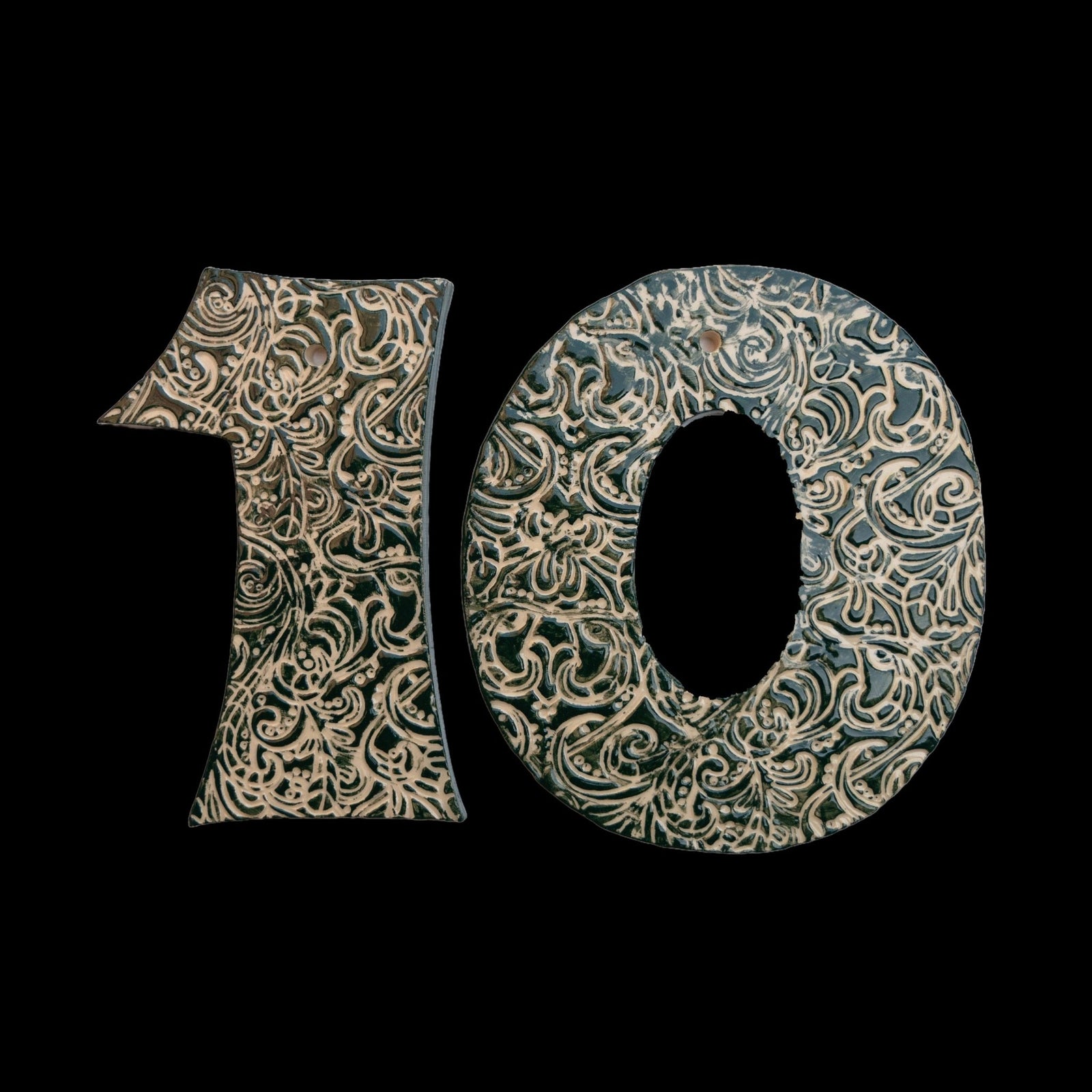 Handgefertigte Keramik-Hausnummer „10“ in Dunkelgrün mit beigefarbenen Ornamentmustern, vor schwarzem Hintergrund dargestellt.