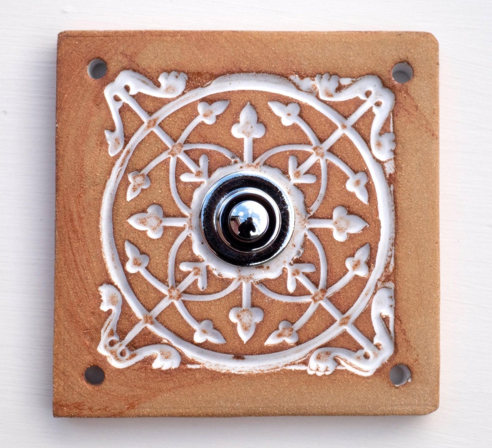 Quadratische Keramikklingel in Goldbraun mit geprägtem weißem Mandala-Muster und silbernem Druckknopf in der Mitte