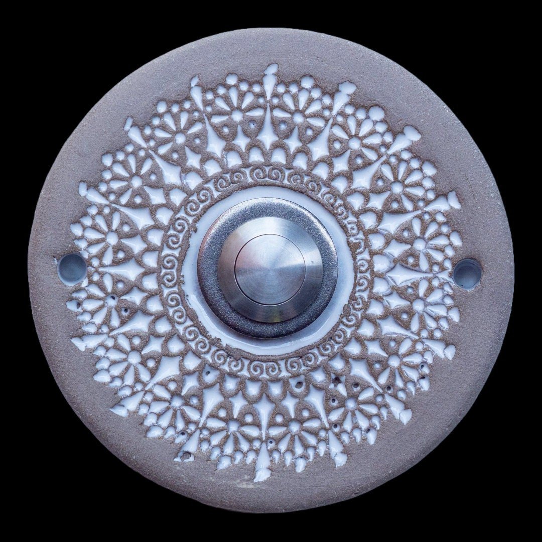 Runde Keramikklingel mit filigranem, spitzenartigem Blumenmuster in Weiß und zentralem silbernen Knopf