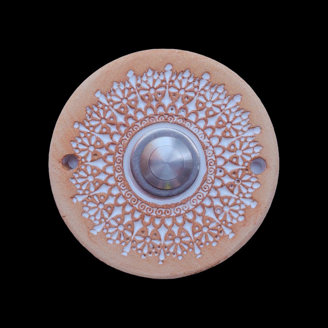 Runde Keramikklingel mit filigranem, spitzenartigem Blumenmuster in Weiß und zentralem silbernen Knopf