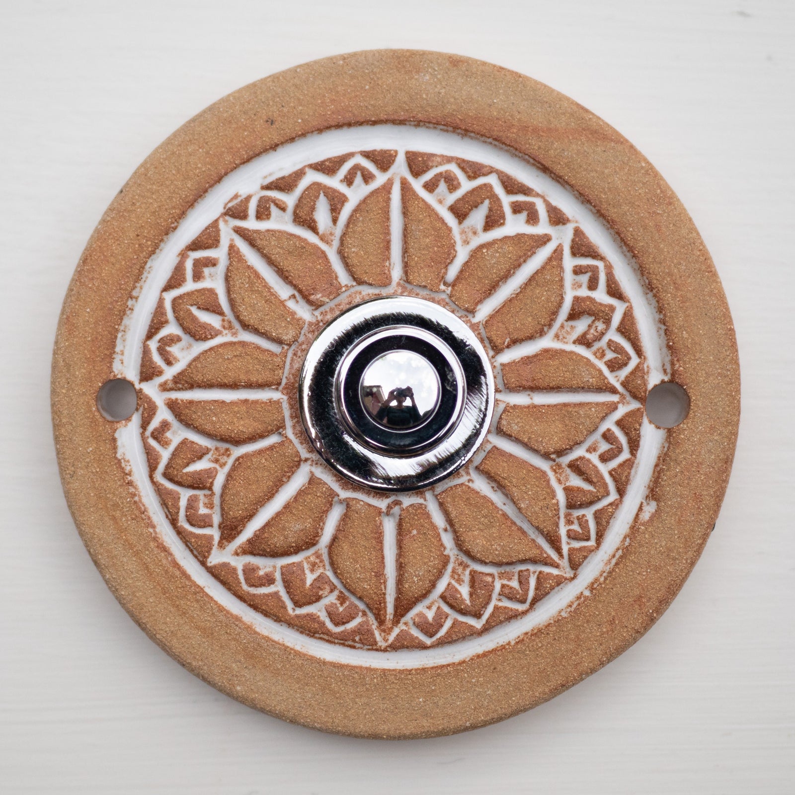 Runde dekorative Klingel mit geprägtem weißem Mandala-Blumenmuster auf goldbrauner Platte und silbernem Druckknopf in der Mitte