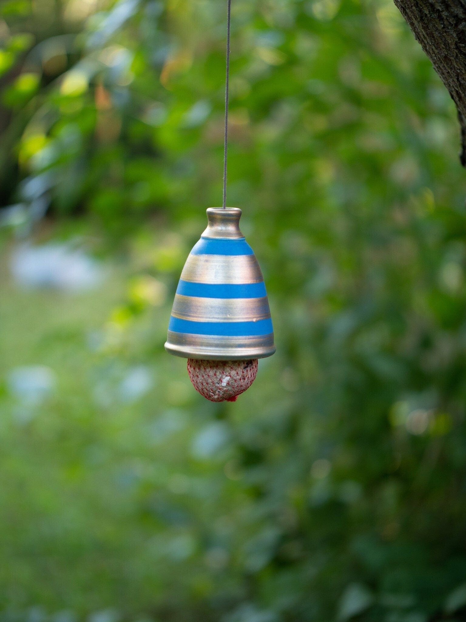 Handgefertigte Meisenknödel-Halterung aus Keramik mit blauen Streifen, hängend im Garten; schützt den Meisenknödel vor Regen und ist frostfest.