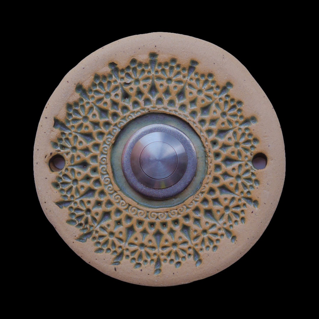 Runde Keramikklingel mit filigranem, spitzenartigem Blumenmuster in Weiß und zentralem silbernen Knopf