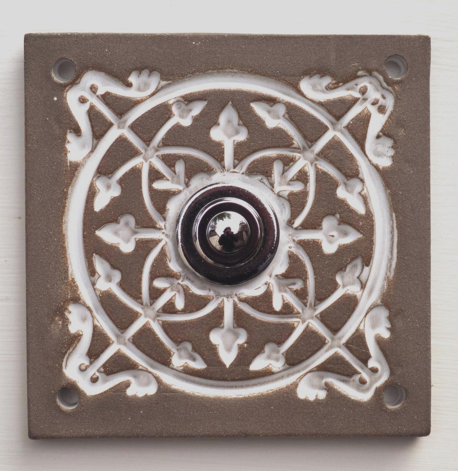 Quadratische Keramikklingel in Grau mit geprägtem weißem Mandala-Muster und silbernem Druckknopf in der Mitte