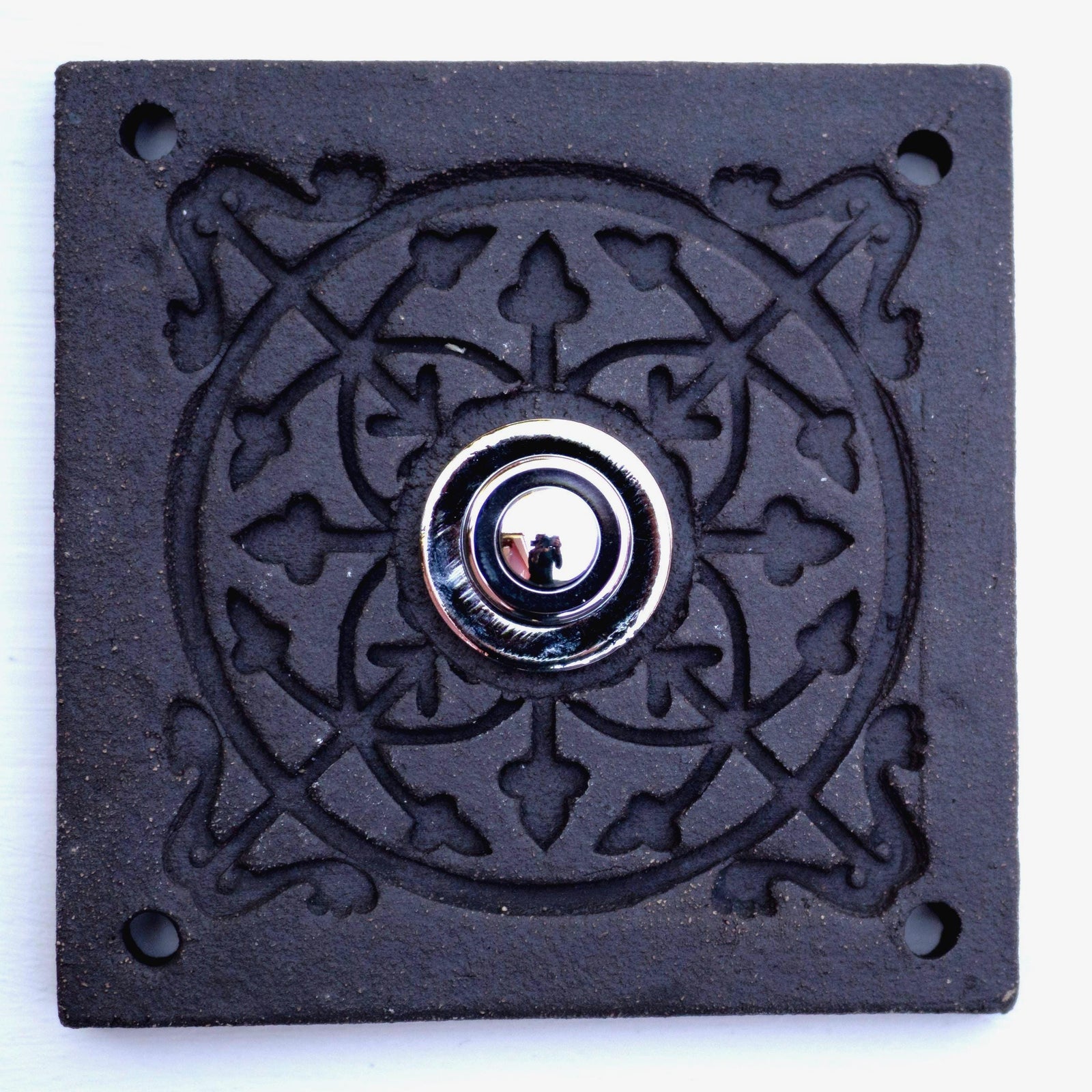Quadratische Keramikklingel in Rein-Schwarz mit geprägtem Mandala-Muster und silbernem Druckknopf in der Mitte.