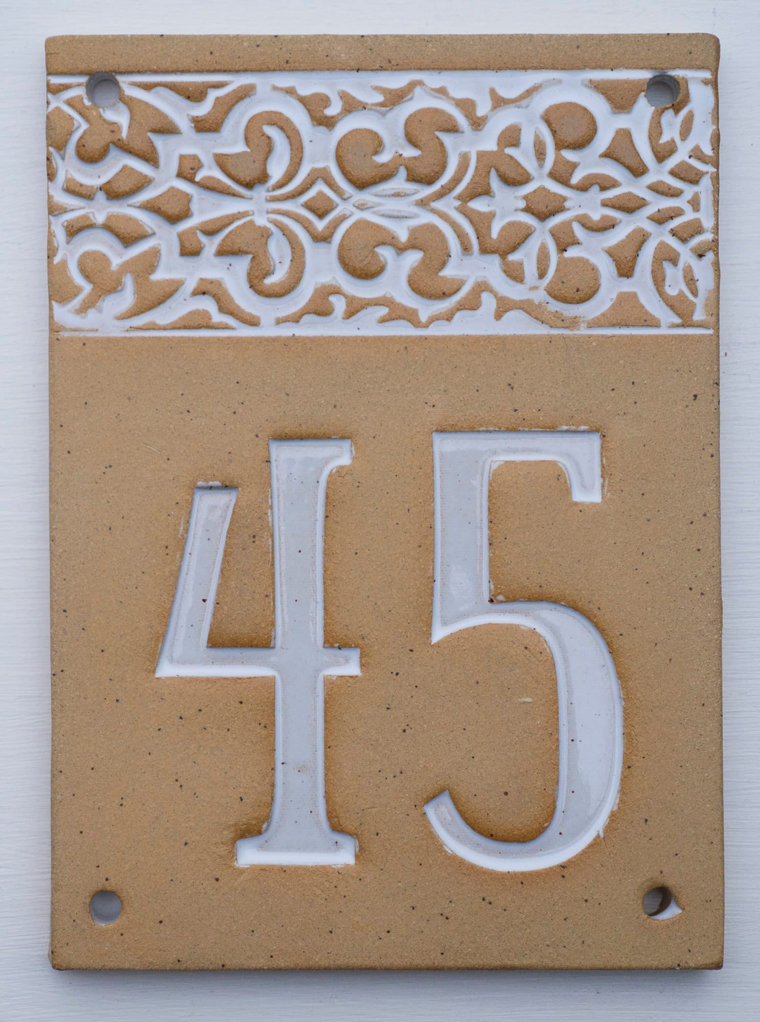 Vertikales rechteckiges Keramik-Hausschild mit beigem Hintergrund, weißen Reliefziffern 45 und dekorativem weißen Fries am oberen Rand