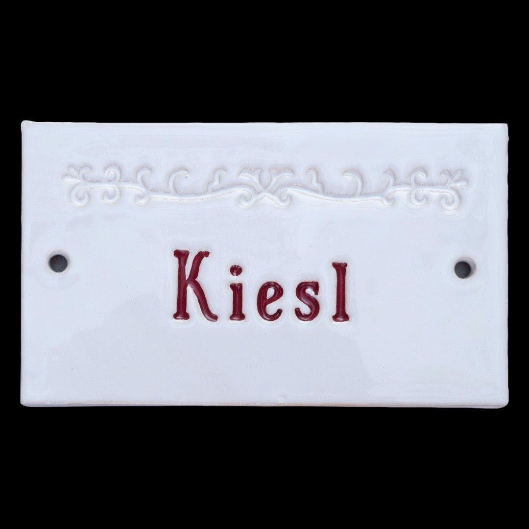 Handgefertigtes weißes Namensschild mit roter Inschrift Kiesl und Zierornament
