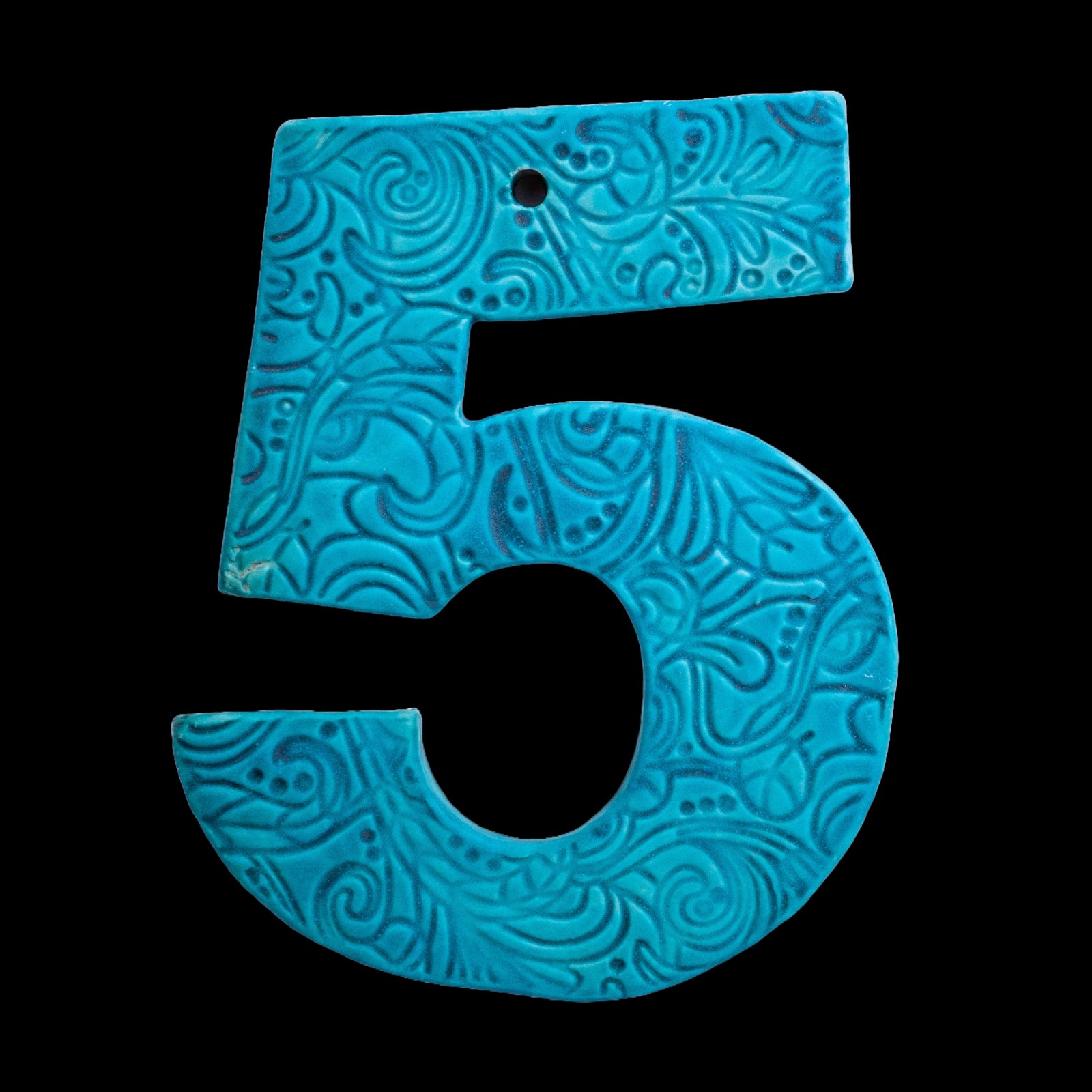 Handgefertigte Keramik-Hausnummer „5“ in Türkisblau mit geprägtem Ornamentmuster, vor schwarzem Hintergrund dargestellt.