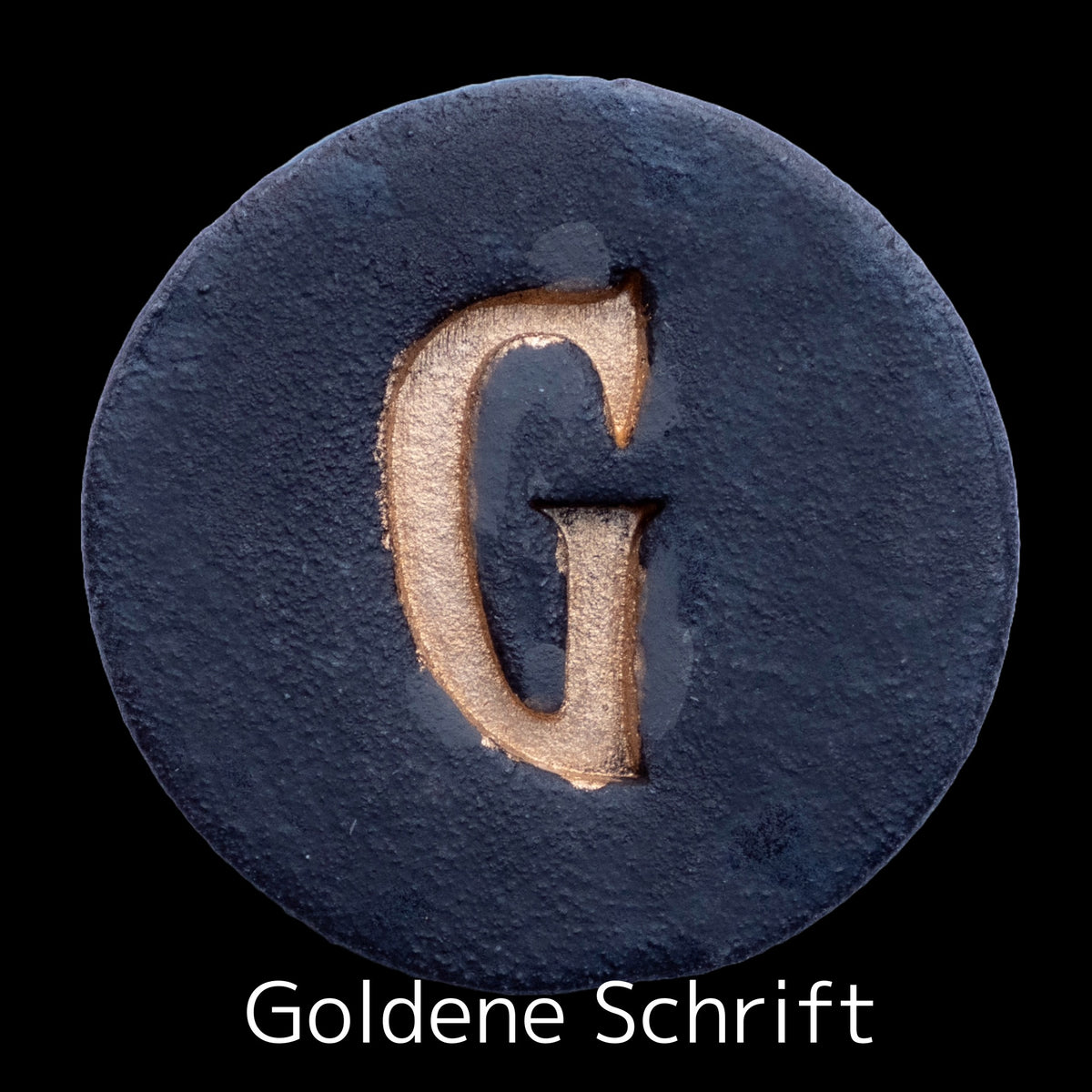Runde dunkle Keramikplatte mit graviertem goldenem Buchstaben G in der Mitte, beschriftet mit &#39;Goldene Schrift&#39;