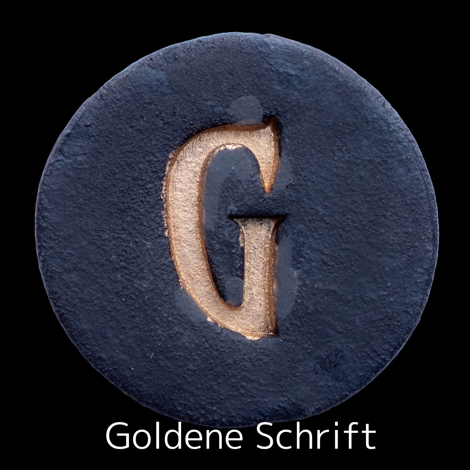 Runde dunkle Keramikplatte mit graviertem goldenem Buchstaben G in der Mitte, beschriftet mit 'Goldene Schrift'