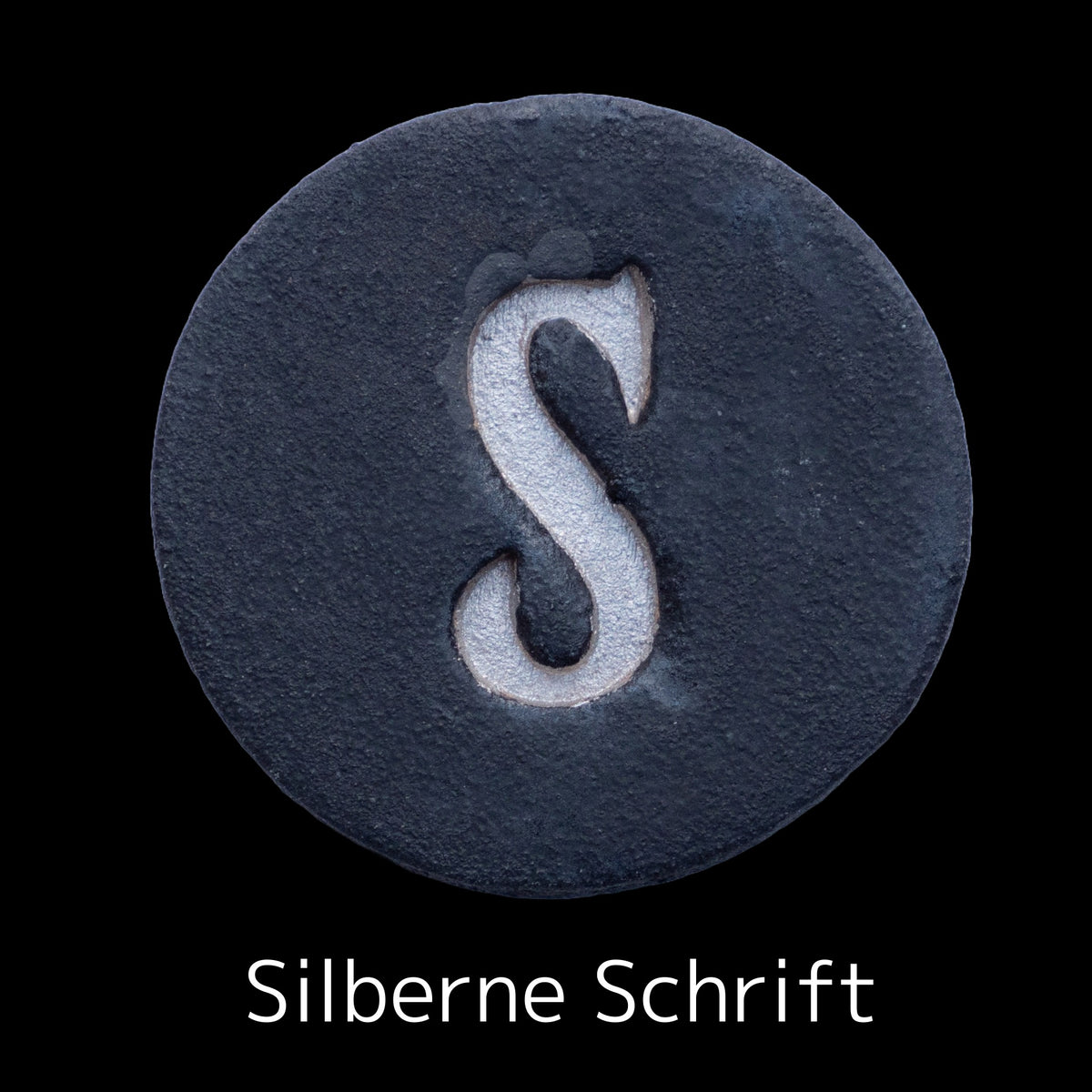 Runde dunkle Keramikplatte mit graviertem silbernen Buchstaben S in der Mitte, beschriftet mit &#39;Silberne Schrift
