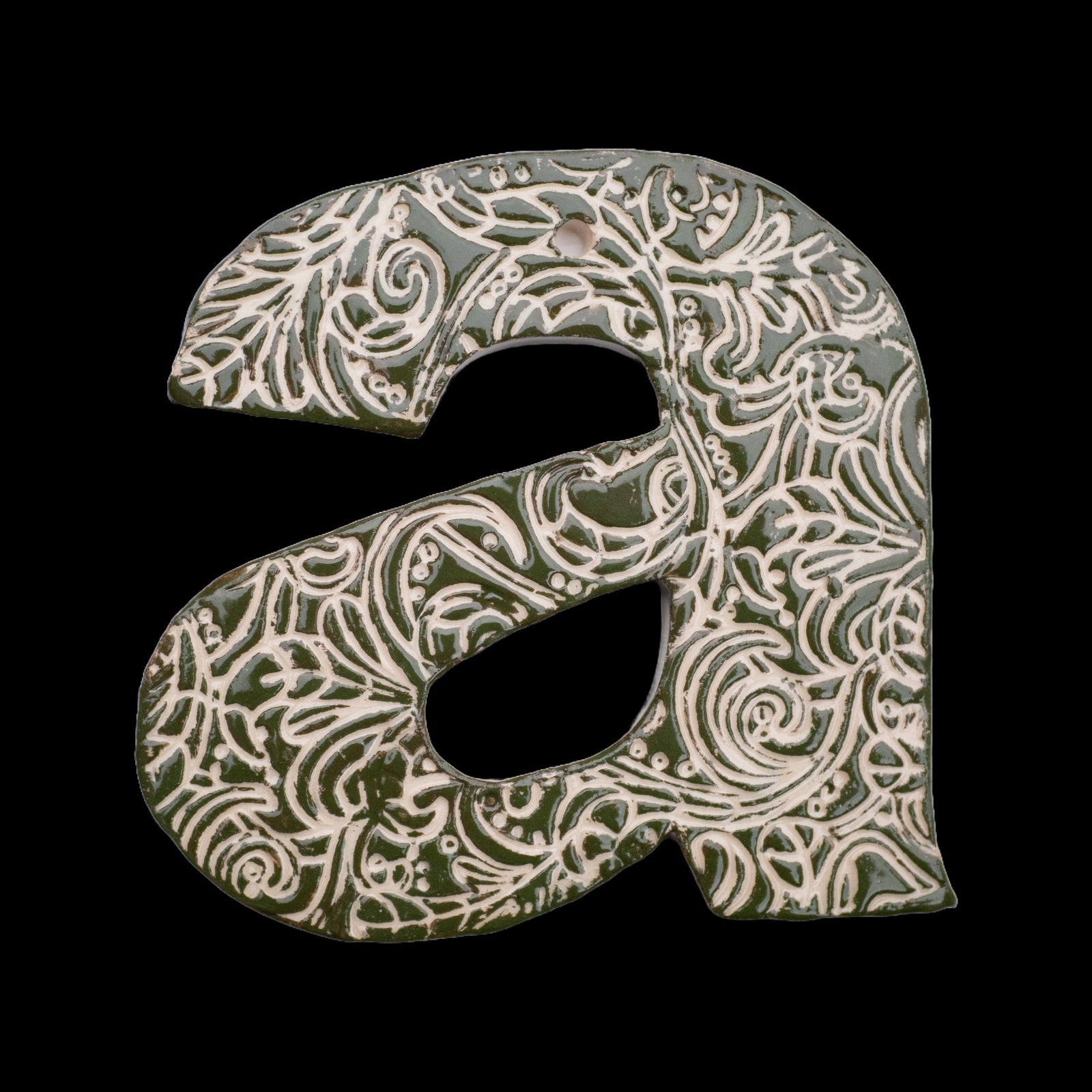 Handgefertigter Keramik-Hausbuchstabe „A“ in Dunkelgrün mit beigefarbenen Ornamentmustern, vor schwarzem Hintergrund dargestellt.
