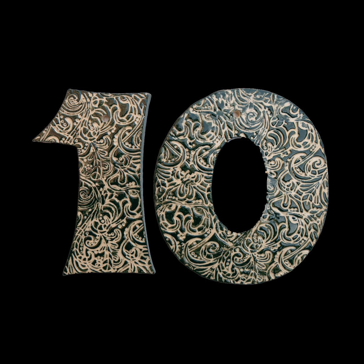 Handgefertigte Keramik-Hausnummer „10“ in Dunkelgrün mit beigefarbenen Ornamentmustern, vor schwarzem Hintergrund dargestellt.