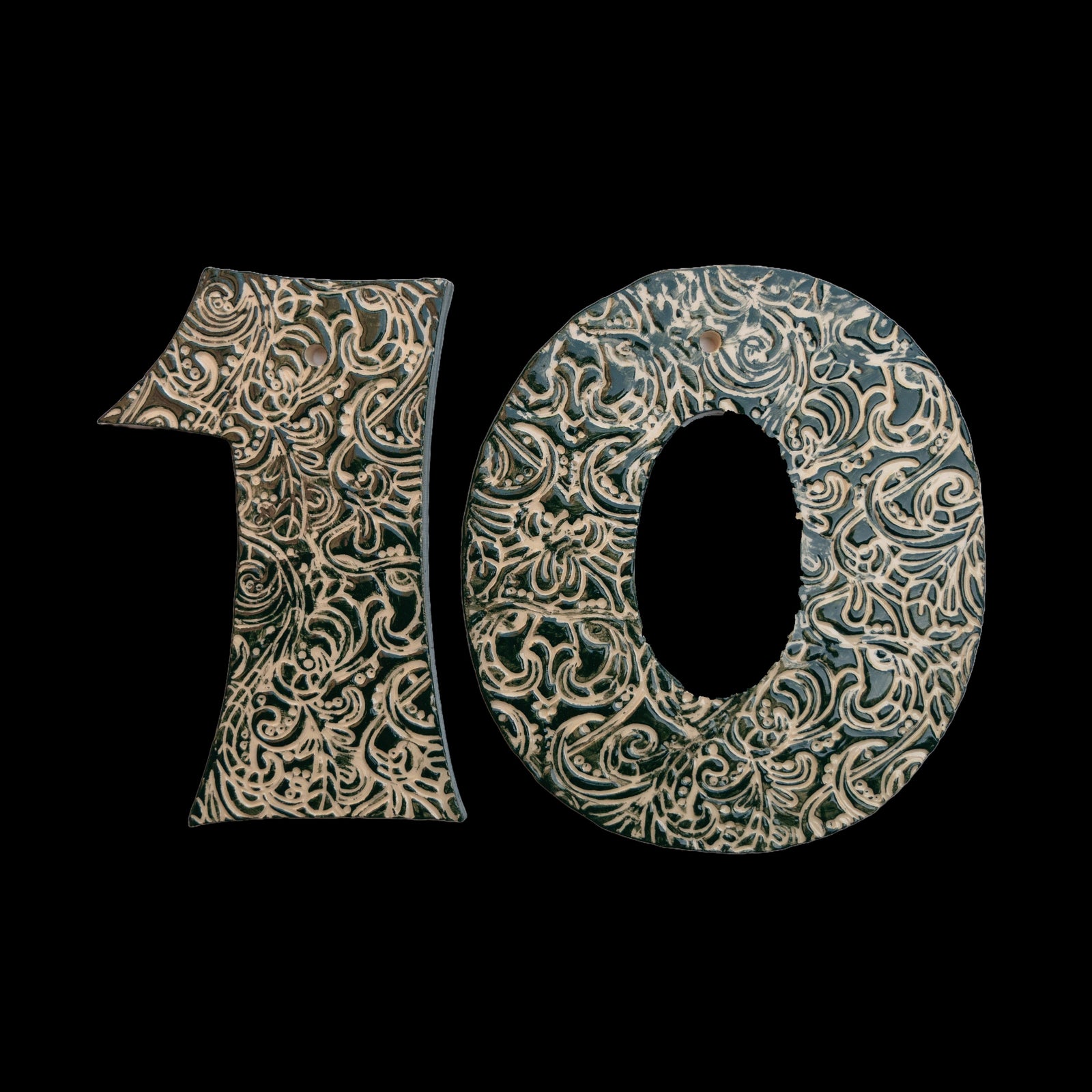 Handgefertigte Keramik-Hausnummer „10“ in Dunkelgrün mit beigefarbenen Ornamentmustern, vor schwarzem Hintergrund dargestellt.