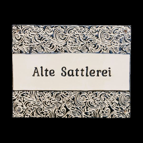 Handgefertigtes Keramikschild mit ornamentalem Schwarz-Weiß-Design und der Aufschrift „Alte Sattlerei“. Elegant und wetterfest für den Außenbereich.