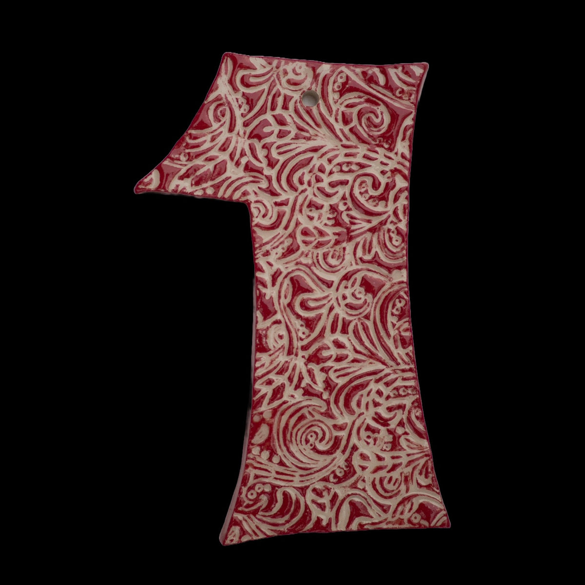 Handgefertigte Keramik-Hausnummer „1“ in Rot mit weißen Ornamentmustern, vor schwarzem Hintergrund dargestellt.