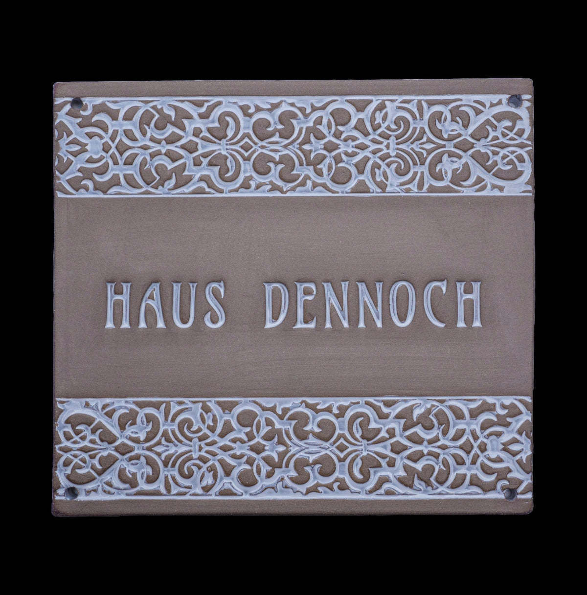 Rechteckiges dekoratives Hausschild mit verzierten floralen Mustern am oberen und unteren Rand und der Gravur „Haus Dennoch“ in der Mitte.