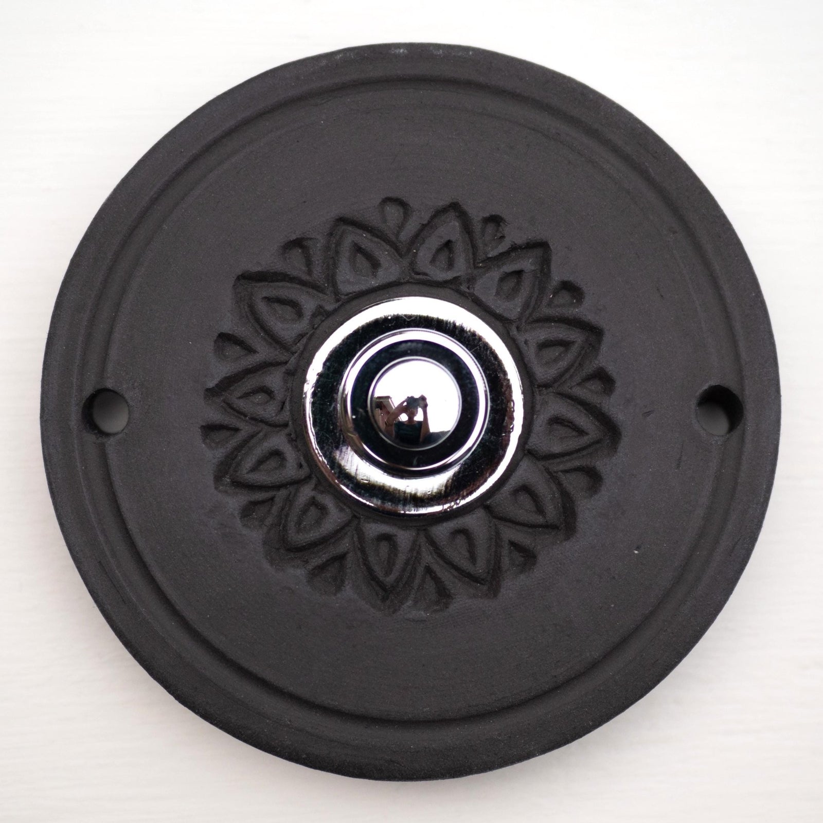 Runde dekorative Klingel mit geprägtem Blumen-Sternmuster auf schwarzer Platte und silbernem Druckknopf in der Mitte.