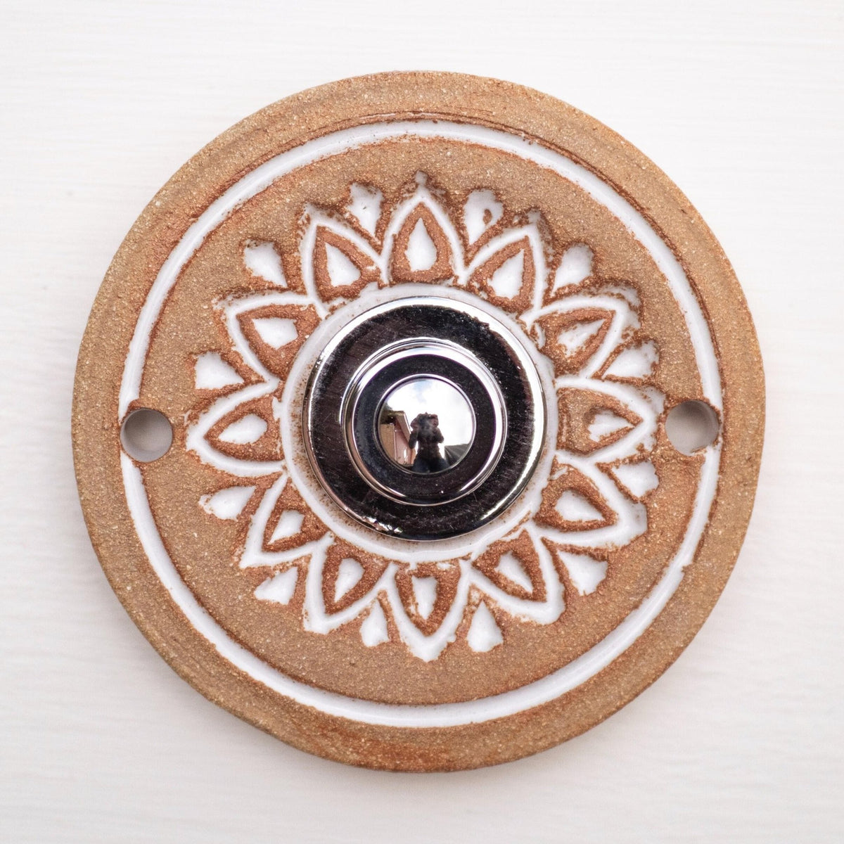 Runde dekorative Klingel mit weißem geprägtem Blumen-Sternmuster auf goldbrauner Platte und silbernem Druckknopf in der Mitte.