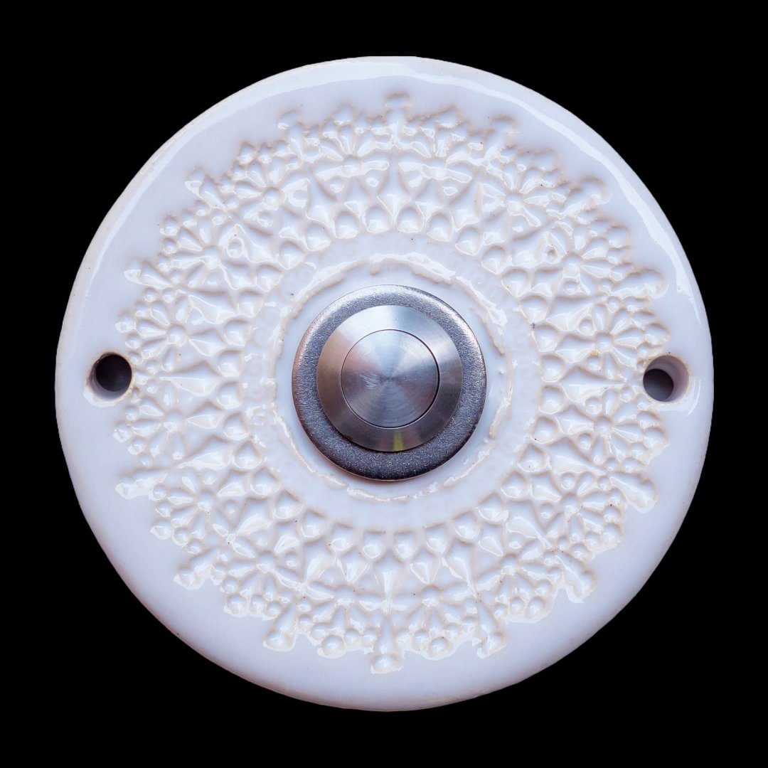 Runde Keramikklingel mit filigranem, spitzenartigem Blumenmuster in Weiß und zentralem silbernen Knopf