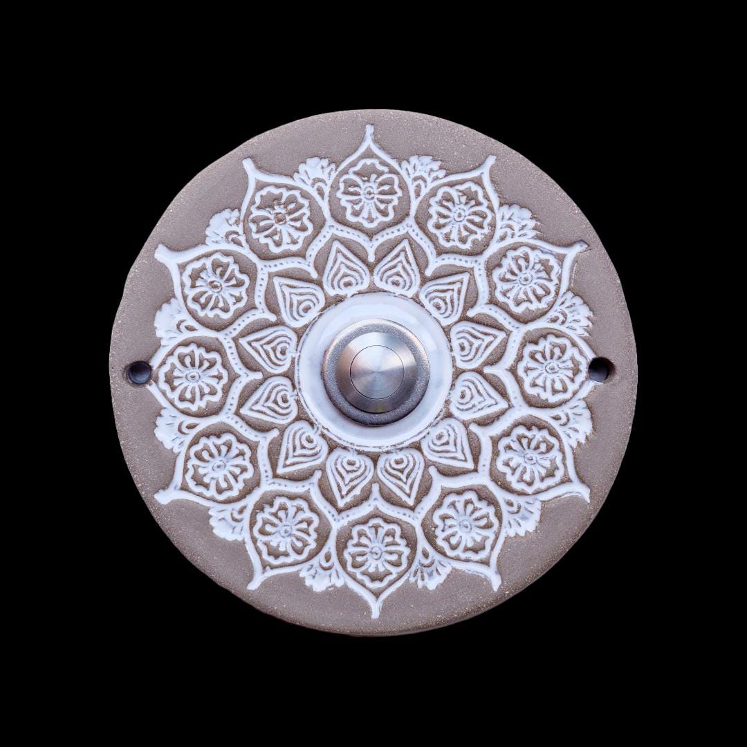Runde Keramikklingel mit filigranem, spitzenartigem Blumenmuster in Weiß und zentralem silbernen Knopf