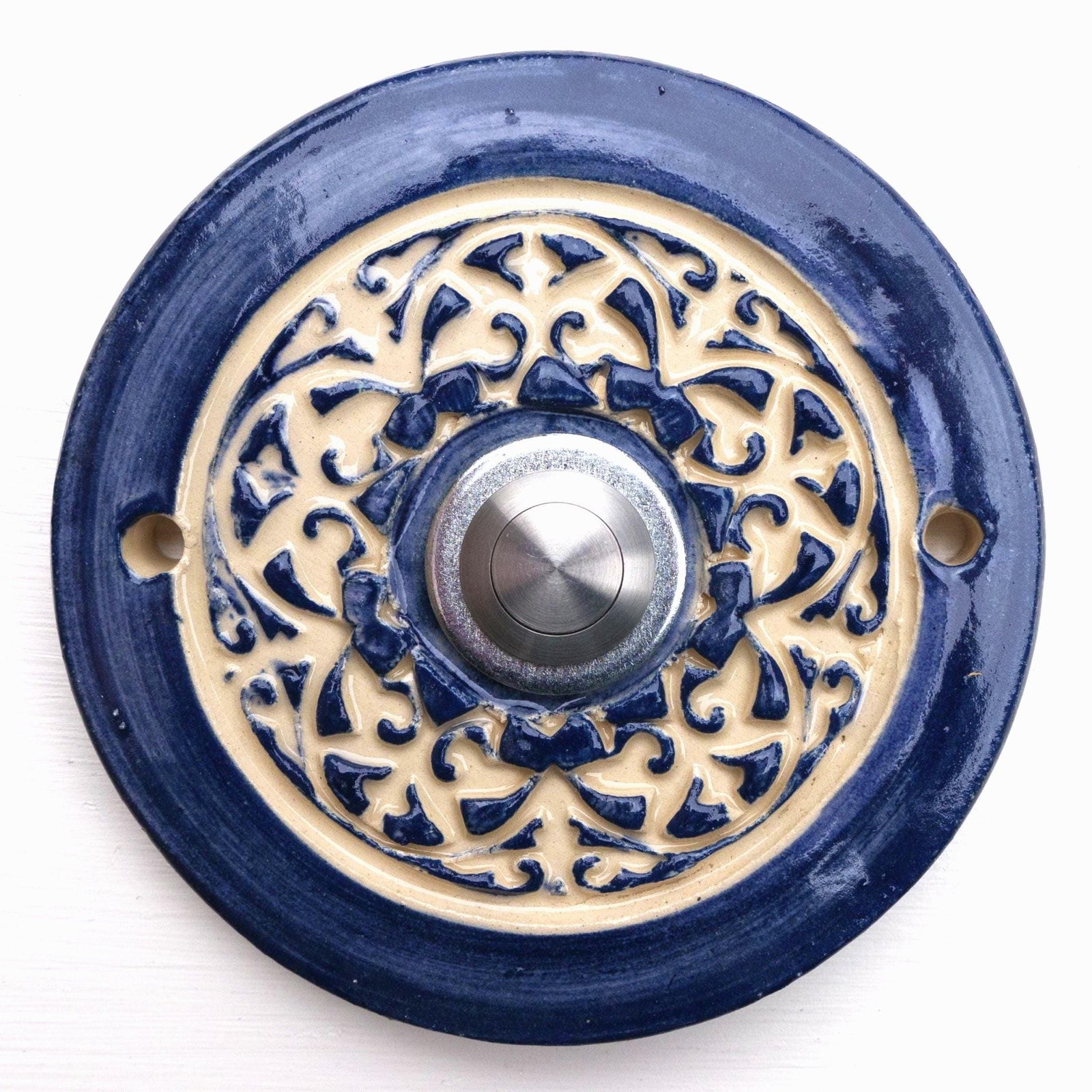 Handgefertigte runde Keramiktürklingel in kräftigem Blau mit kunstvollem cremefarbenem Reliefmuster. Ein zeitloses Stück, das traditionelle Handwerkskunst mit einem modernen Edelstahlknopf verbindet.