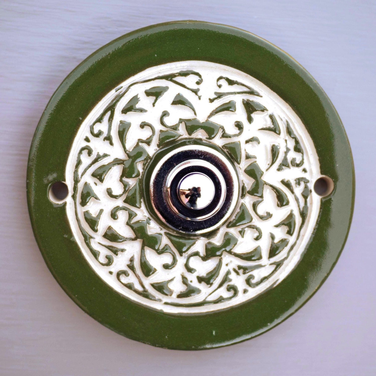 Handgefertigte runde Keramiktürklingel in sattem Grün mit kunstvollem cremefarbenem Reliefmuster. Elegant und langlebig, veredelt mit einem modernen Edelstahlknopf