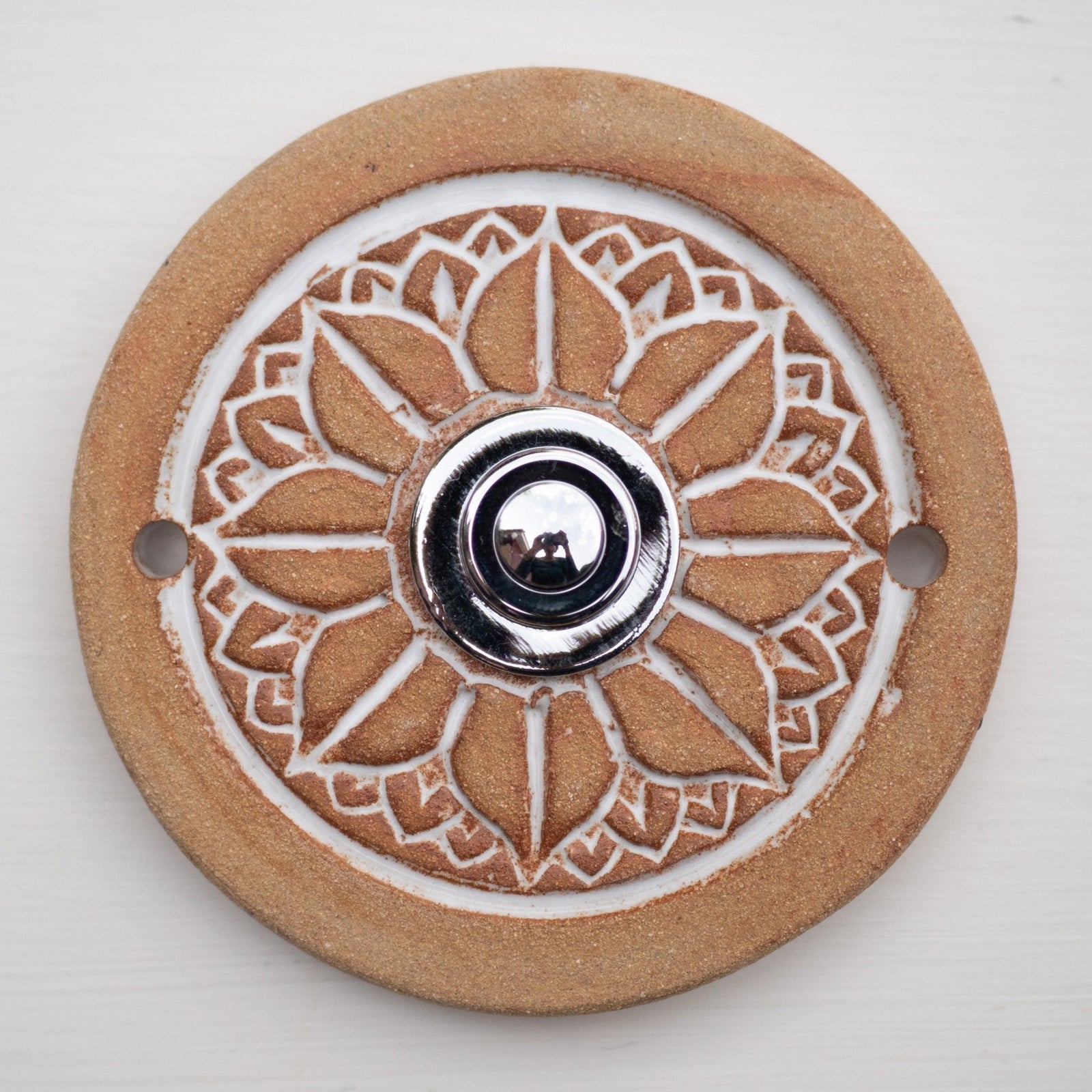 Runde dekorative Klingel mit geprägtem weißem Mandala-Blumenmuster auf goldbrauner Platte und silbernem Druckknopf in der Mitte