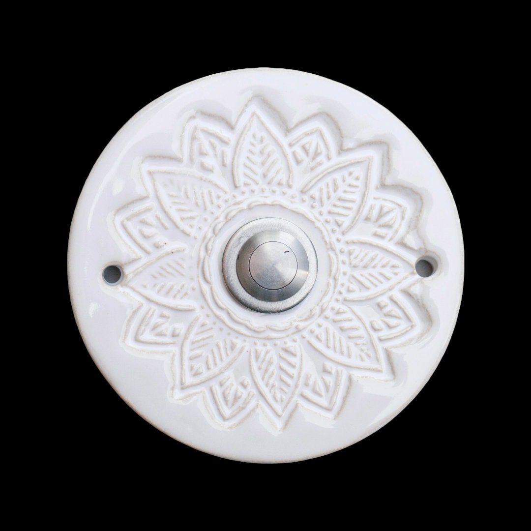 Runde dekorative Klingel mit geprägtem Mandala-Blumenmuster auf glänzender weißer Platte und silbernem Druckknopf in der Mitte