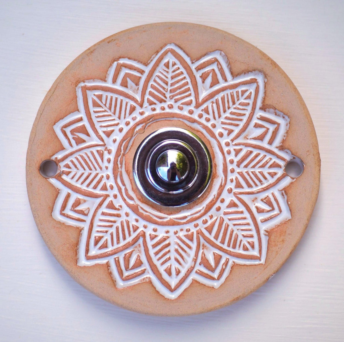 Runde dekorative Klingel mit geprägtem weißem Mandala-Blumenmuster auf goldbrauner Platte und silbernem Druckknopf in der Mitte.