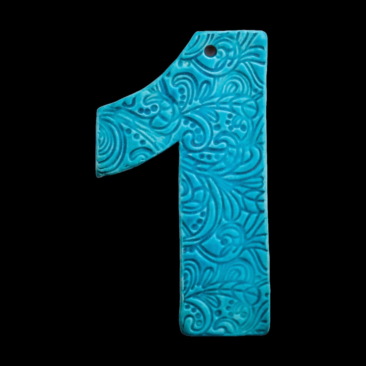 Handgefertigte Keramik-Hausnummer „1“ in Türkisblau mit geprägtem ornamentalen Wirbelmuster, vor schwarzem Hintergrund dargestellt.