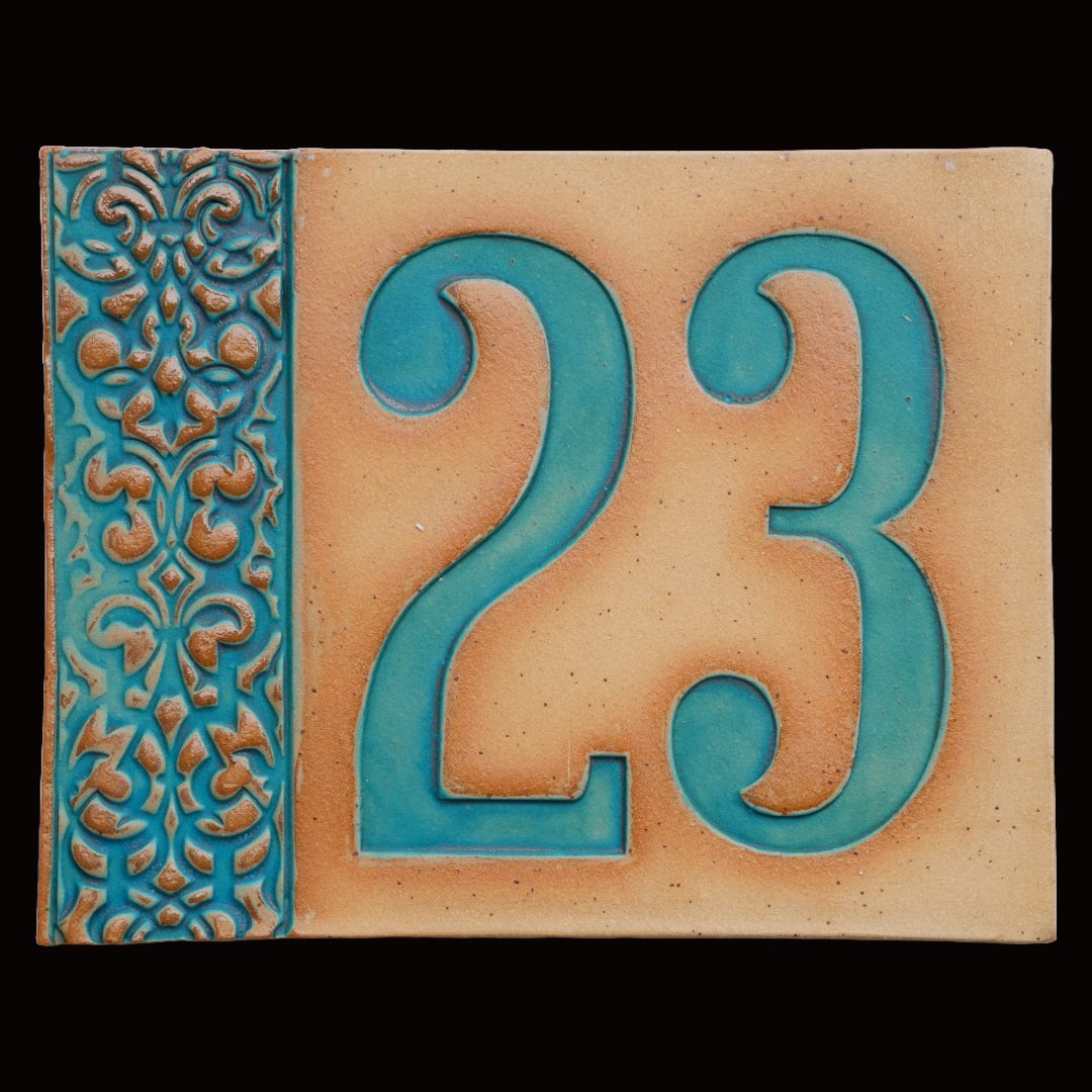 Rechteckiges Keramik-Hausschild mit beigem Hintergrund, türkisfarbenen Reliefziffern 23 und ornamentalem türkisfarbenem Rand auf der linken Seite