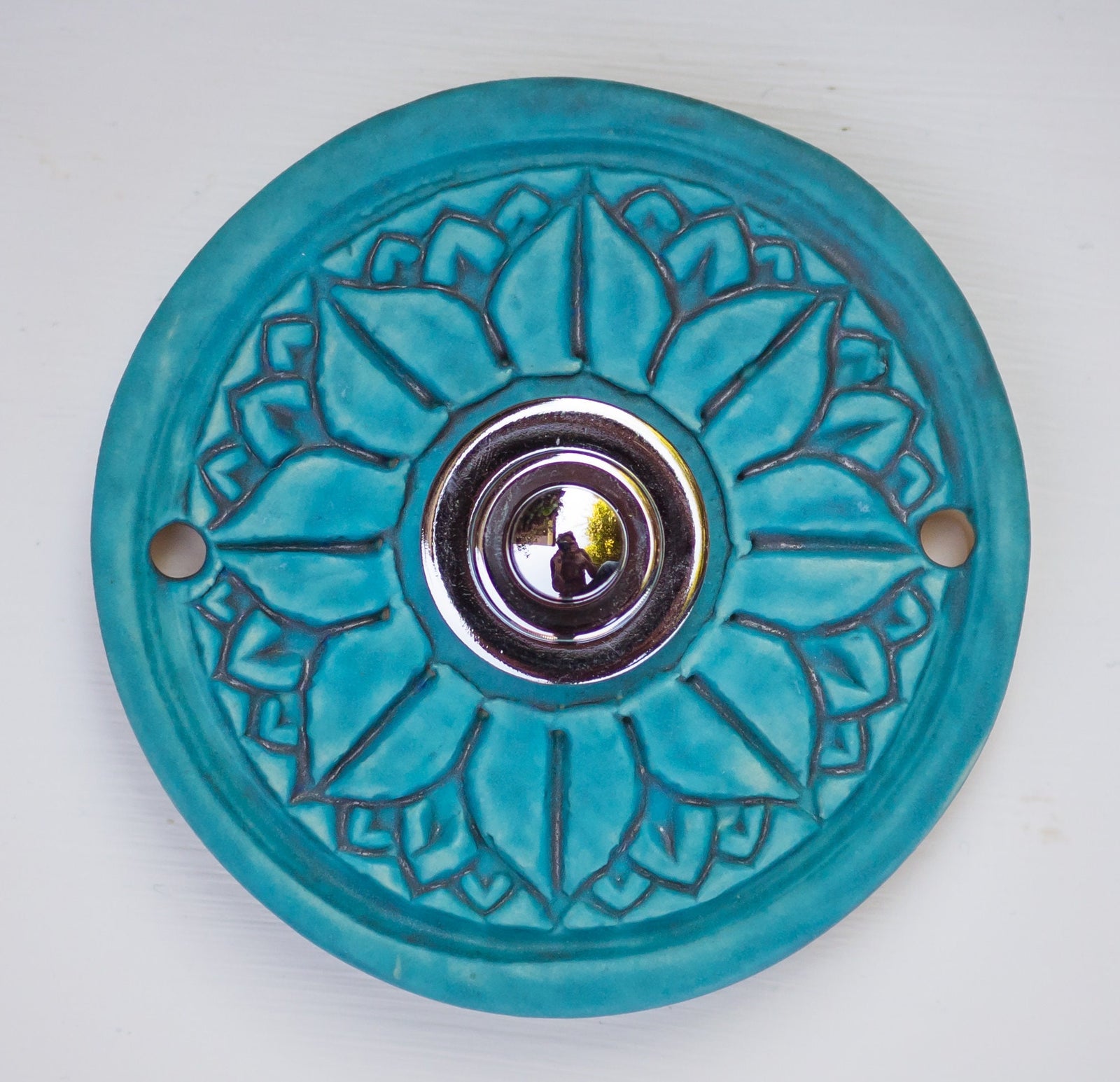 Runde dekorative Klingel mit geprägtem Mandala-Blumenmuster auf leuchtend blauer Platte und silbernem Druckknopf in der Mitte.