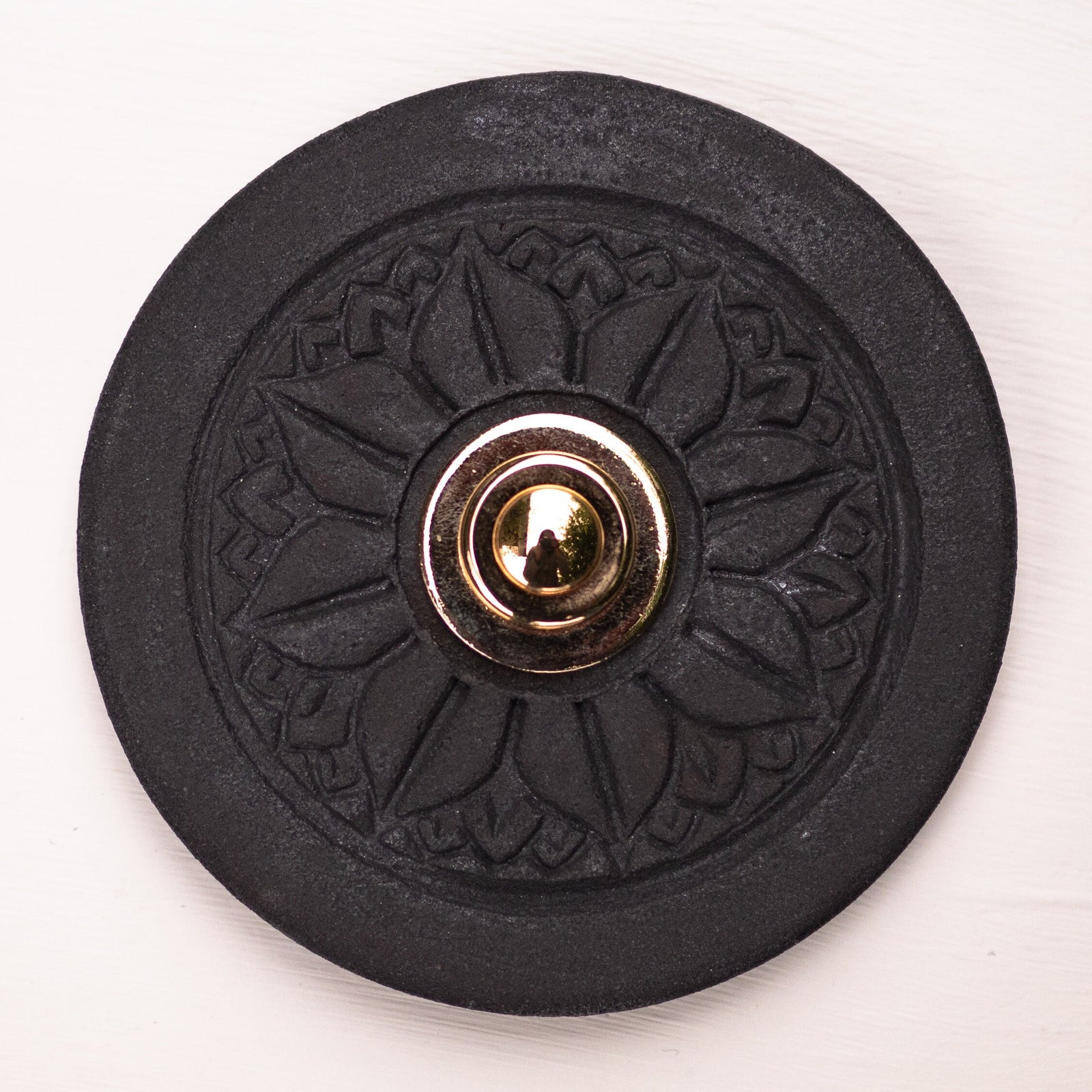 Runde dekorative Klingel mit geprägtem Mandala-Blumenmuster auf schwarzer Platte und silbernem Druckknopf in der Mitte