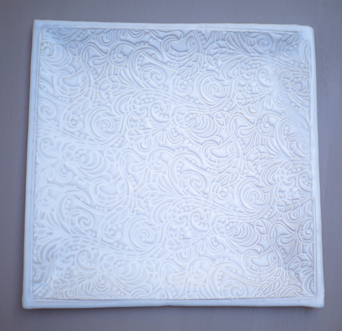 Weiße Keramikfliese mit aufwendig geprägtem Blumen- und Wirbelmuster