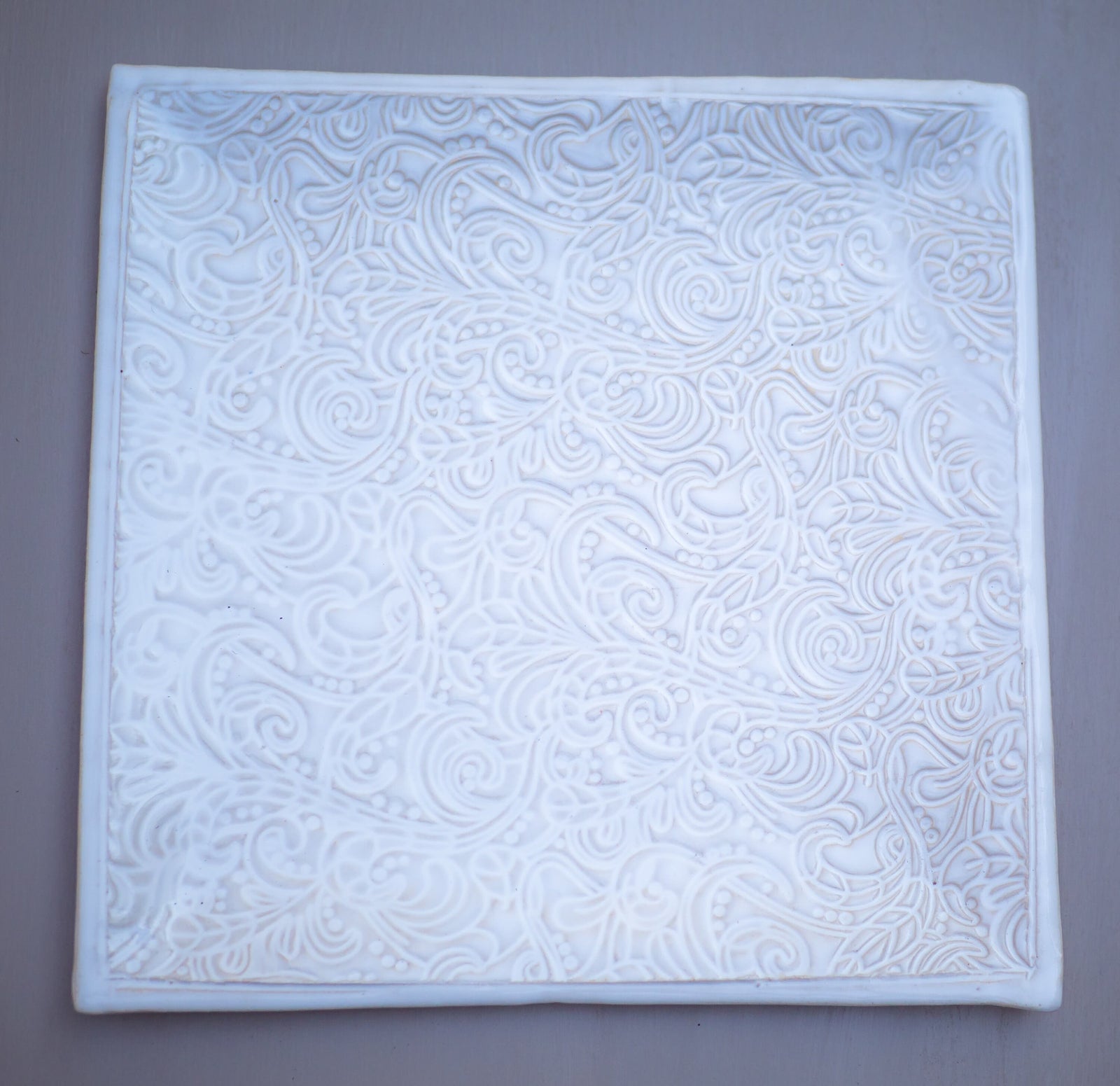 Weiße Keramikfliese mit aufwendig geprägtem Blumen- und Wirbelmuster
