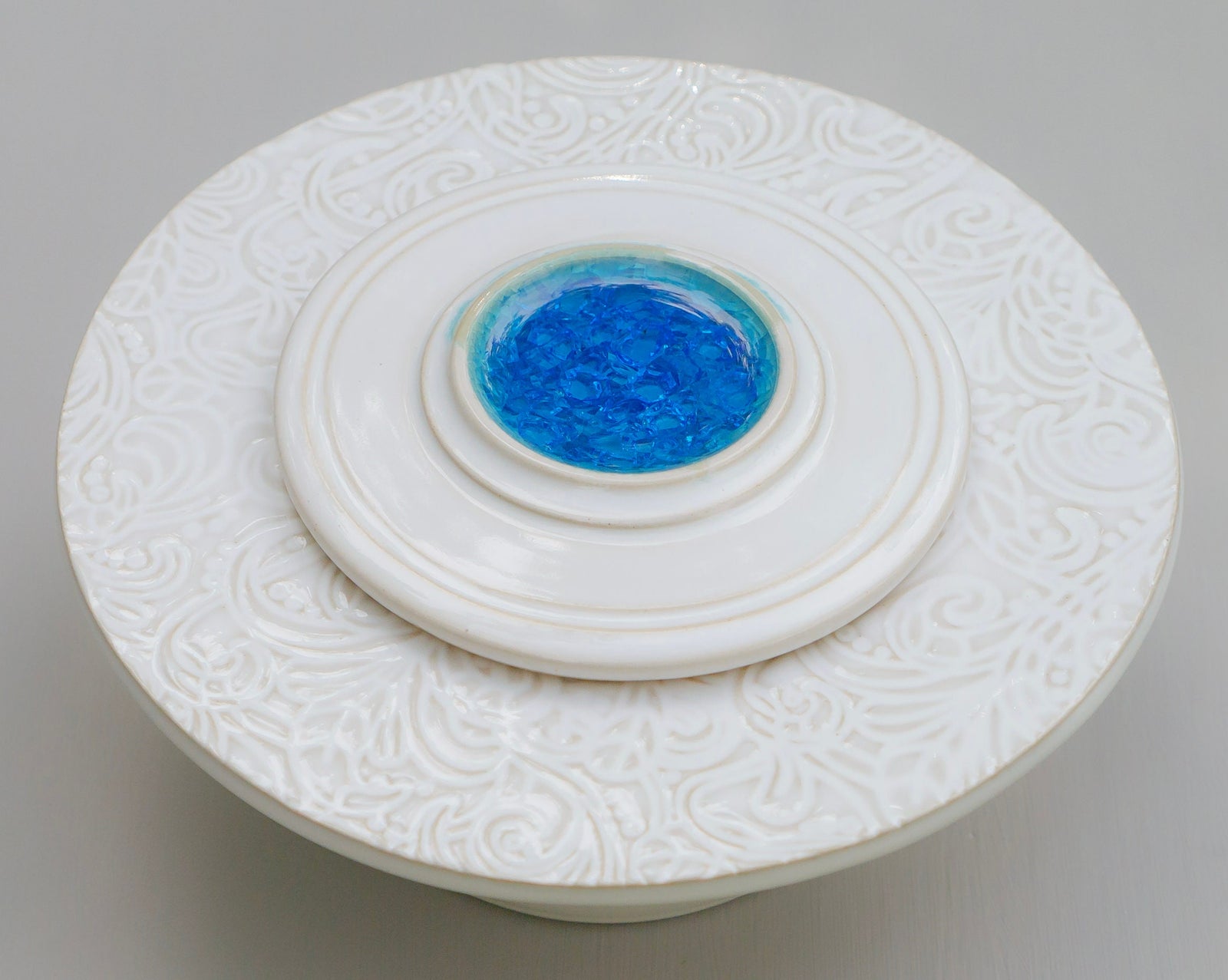 Runde Keramik-Klingelplatte mit geprägtem weißen Wirbelmuster und blauem Glaseinsatz in der Mitte
