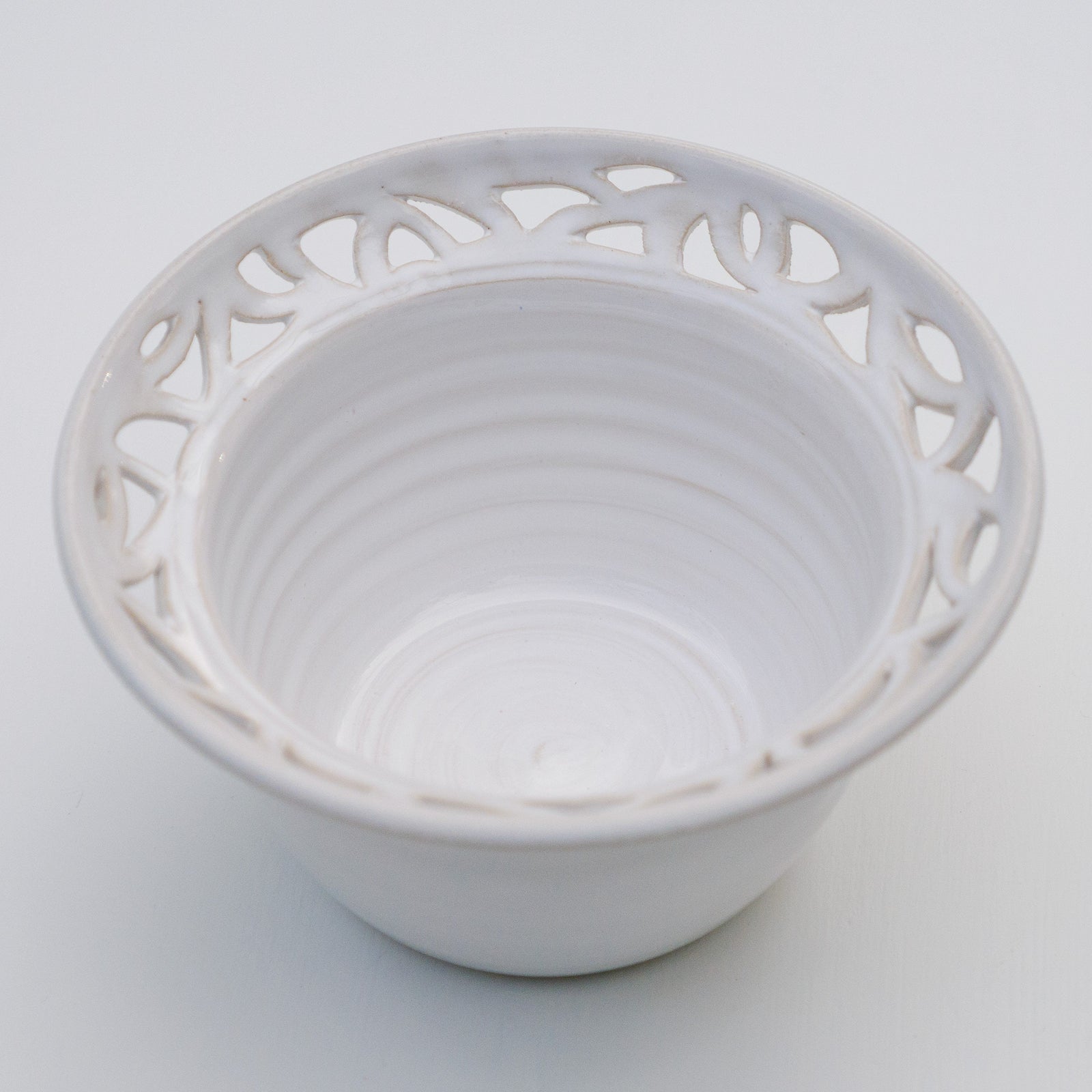 Weiße Keramikschale mit glatten Innenringen und durchbrochenem Rand mit dekorativen Ausschnittmustern.
