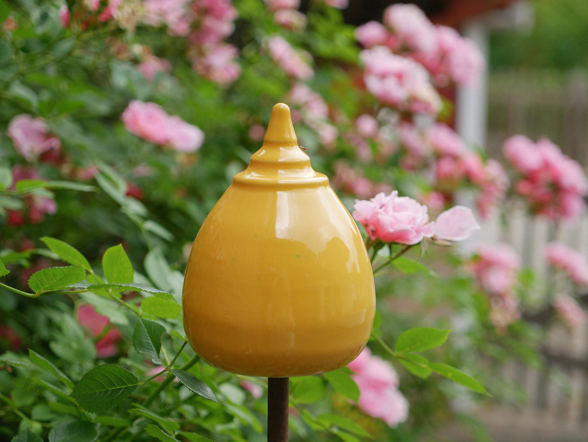 Gelbe Keramik-Gartendekoration in gestufter, glockenähnlicher Form zwischen grünen Pflanzen