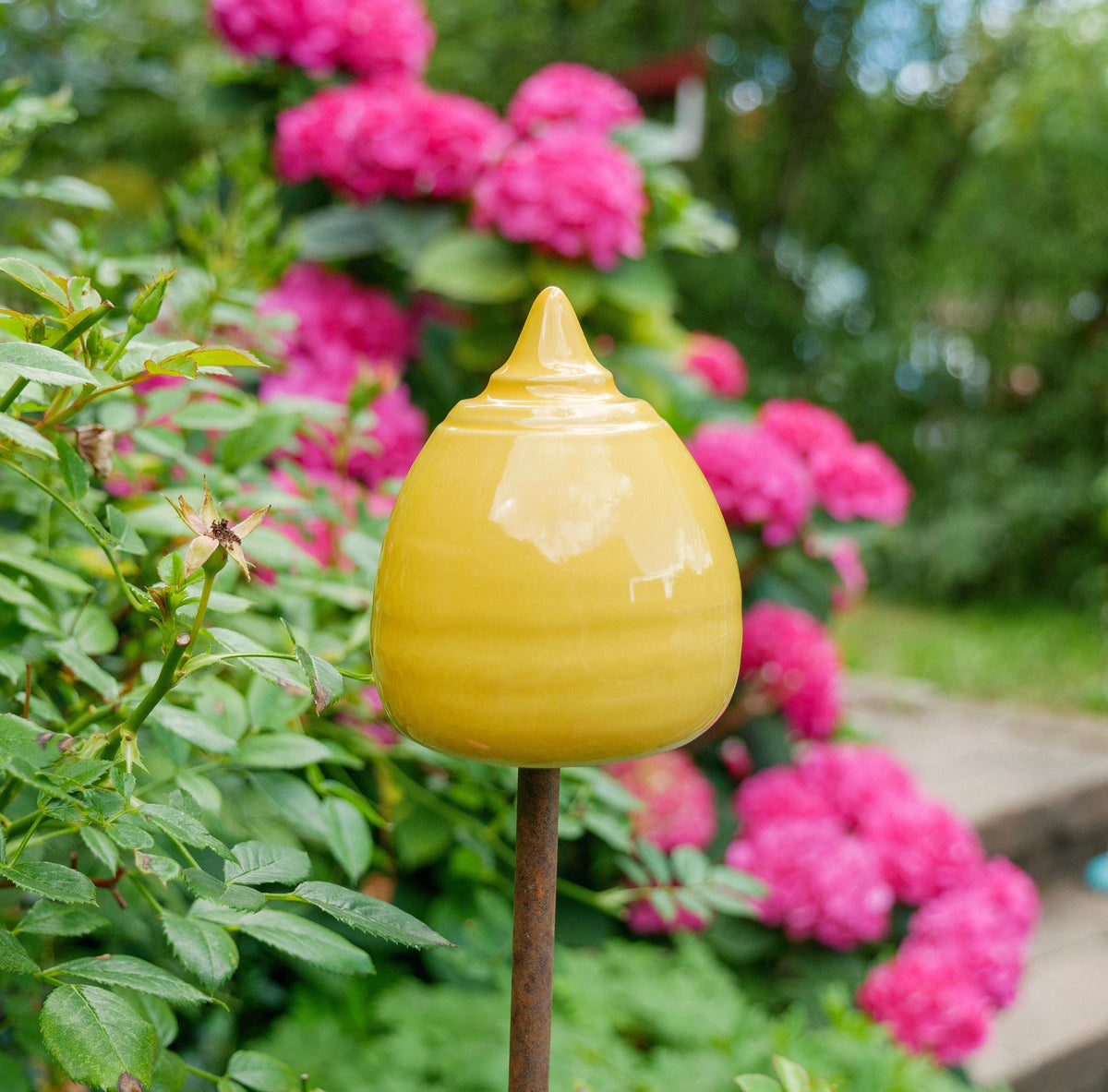 Gelbe Keramik-Gartendekoration in gestufter, glockenähnlicher Form zwischen grünen Pflanzen