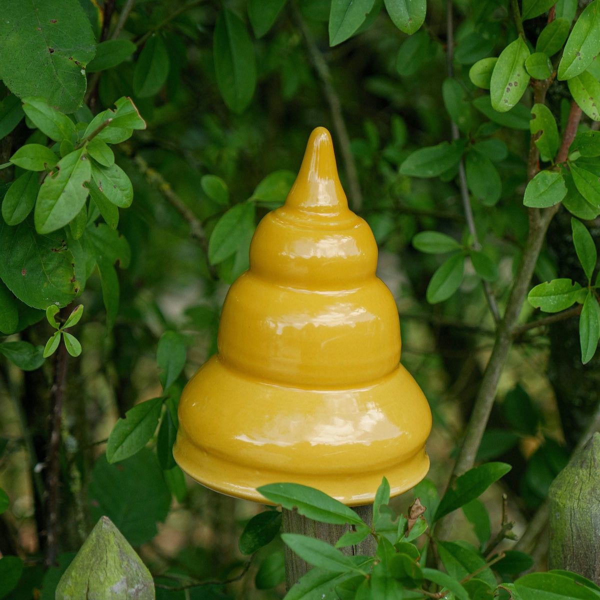 Gelbe Keramik-Gartendekoration in gestufter, glockenähnlicher Form zwischen grünen Pflanzen