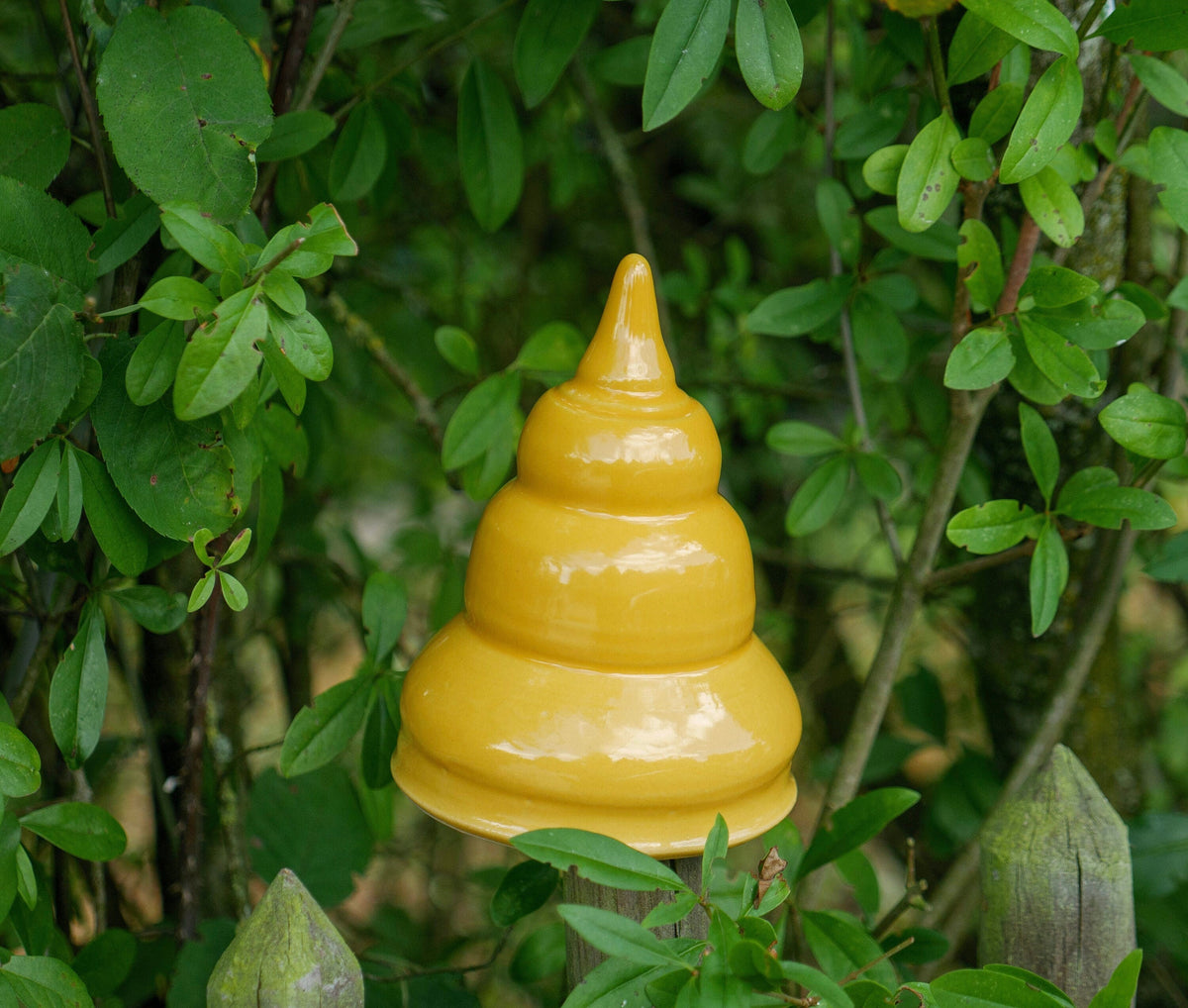 Gelbe Keramik-Gartendekoration in gestufter, glockenähnlicher Form zwischen grünen Pflanzen