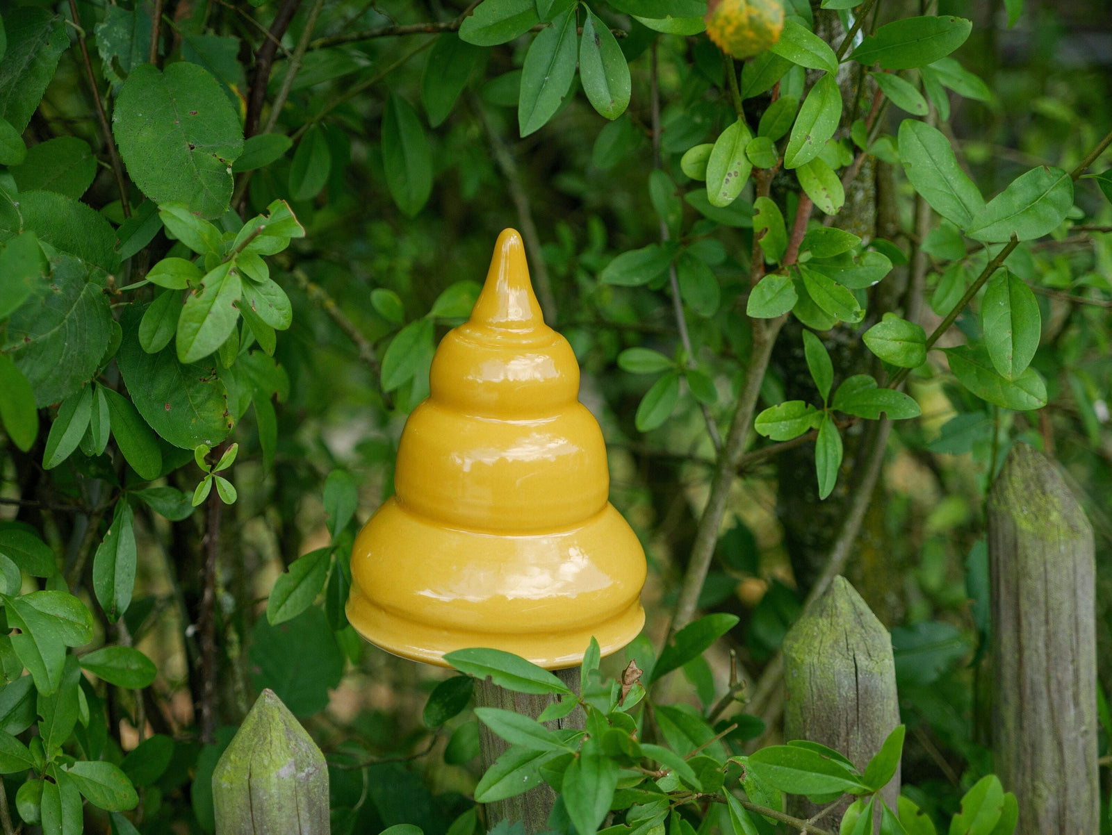 Gelbe Keramik-Gartendekoration in gestufter, glockenähnlicher Form zwischen grünen Pflanzen