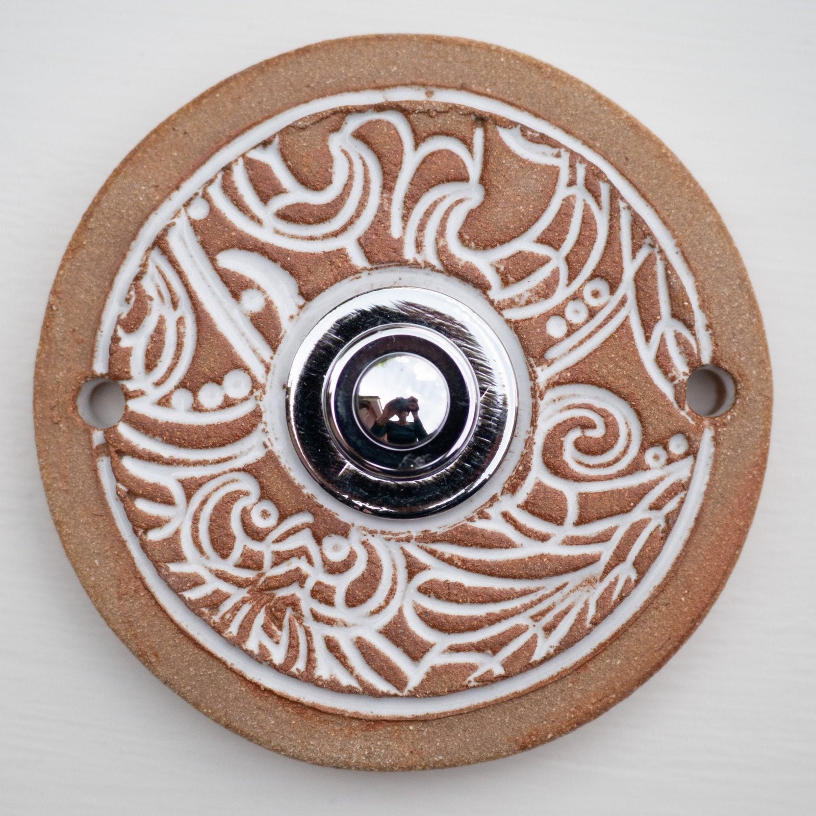 Runde dekorative Klingel mit reinweißem Ornamentmuster auf goldbrauner Platte und silbernem Druckknopf in der Mitte