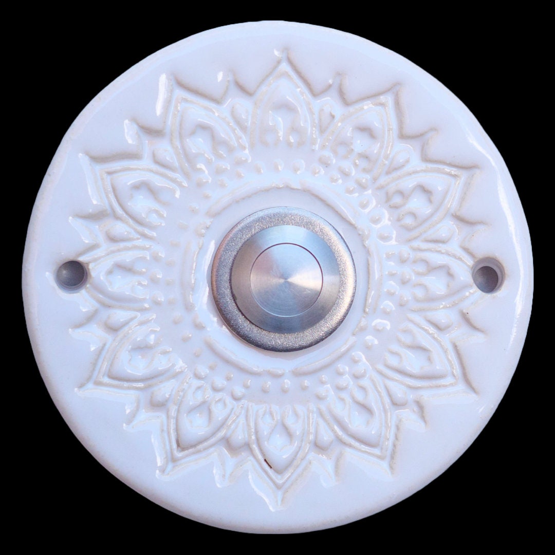 Handgefertigte Keramiktürklingel in elegantem Weiß mit filigranem Mandala-Blumenmuster. Der silberne Knopf setzt einen modernen Akzent und verbindet Tradition mit zeitlosem Design. Eine stilvolle Möglichkeit, Ihre Gäste zu begrüßen.