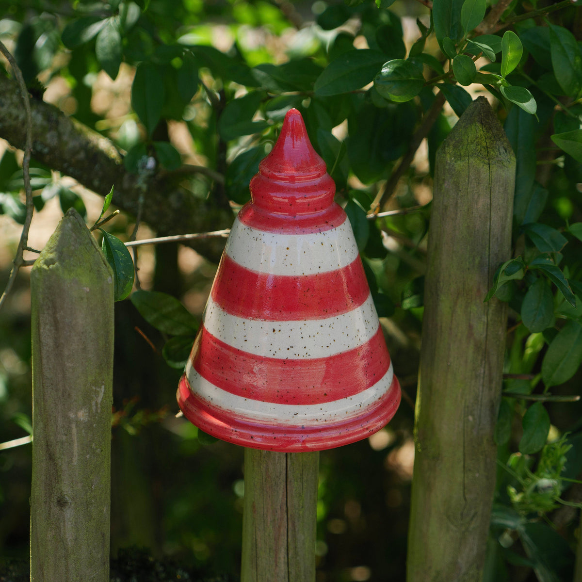 Handgefertigte Keramik-Gartenstele mit roten und weißen Streifen in Kegelform, befestigt auf einem Holzpfosten zwischen grünen Pflanzen