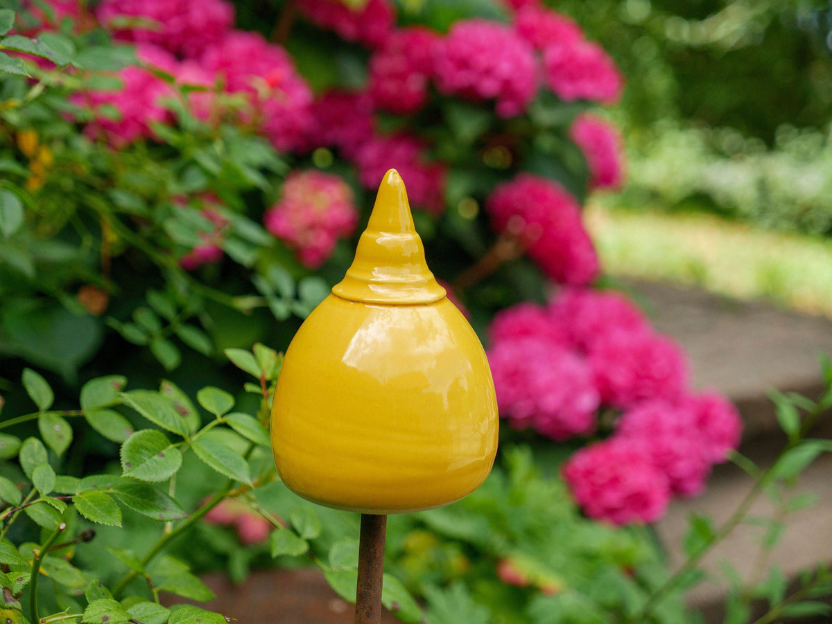 Gelbe Keramik-Gartendekoration in gestufter, glockenähnlicher Form zwischen grünen Pflanzen