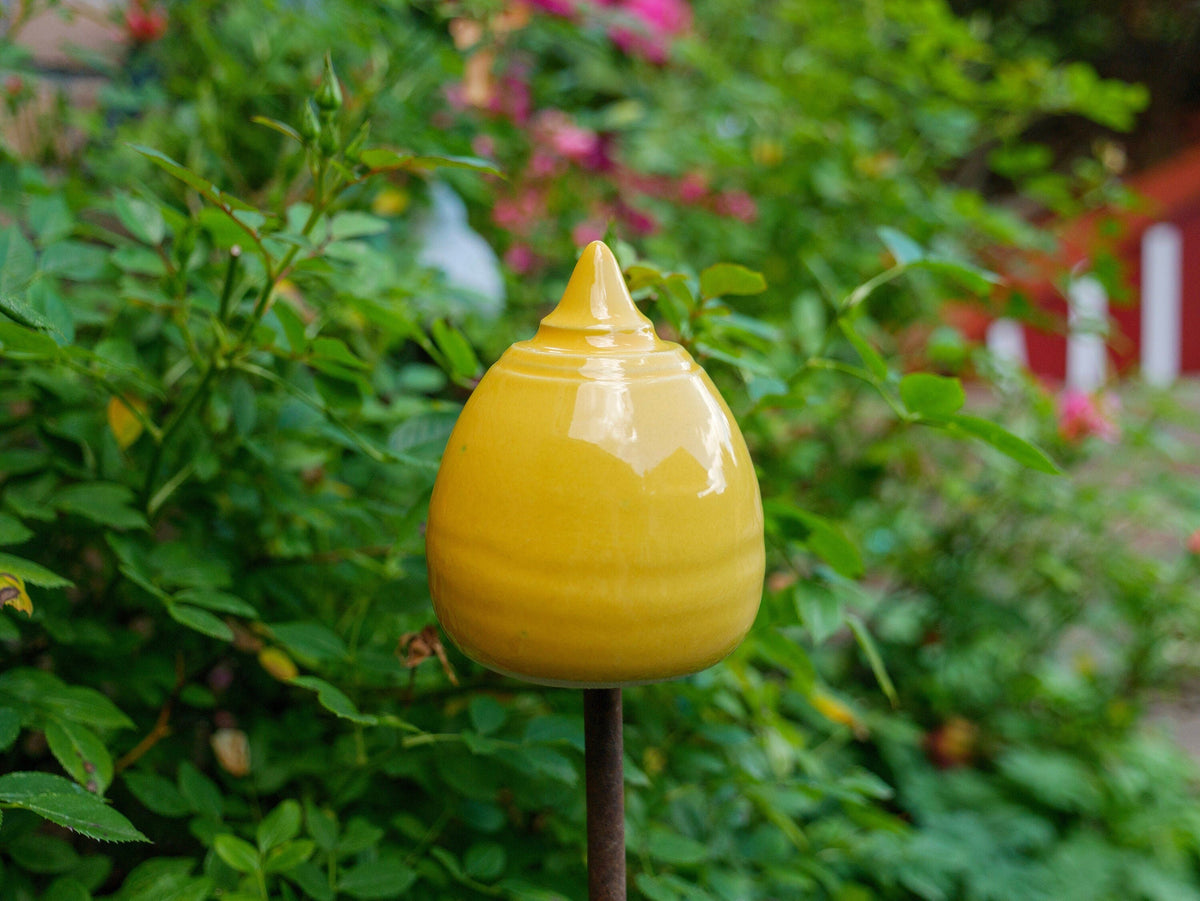 Gelbe Keramik-Gartendekoration in gestufter, glockenähnlicher Form zwischen grünen Pflanzen